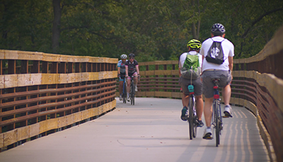 People biking along a boardwalk bridge surrounded by trees